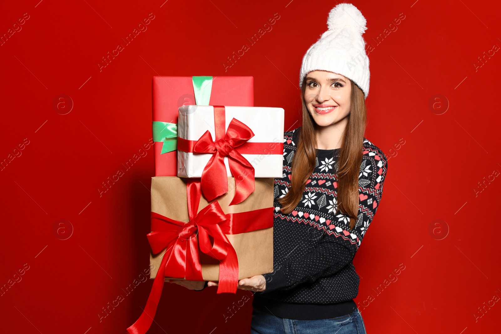 Photo of Young woman in Christmas sweater holding gift boxes on red background