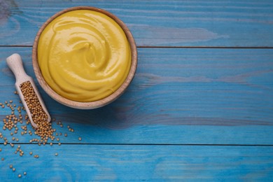 Photo of Sauce bowl with delicious mustard and seeds on light blue wooden table, flat lay. Space for text