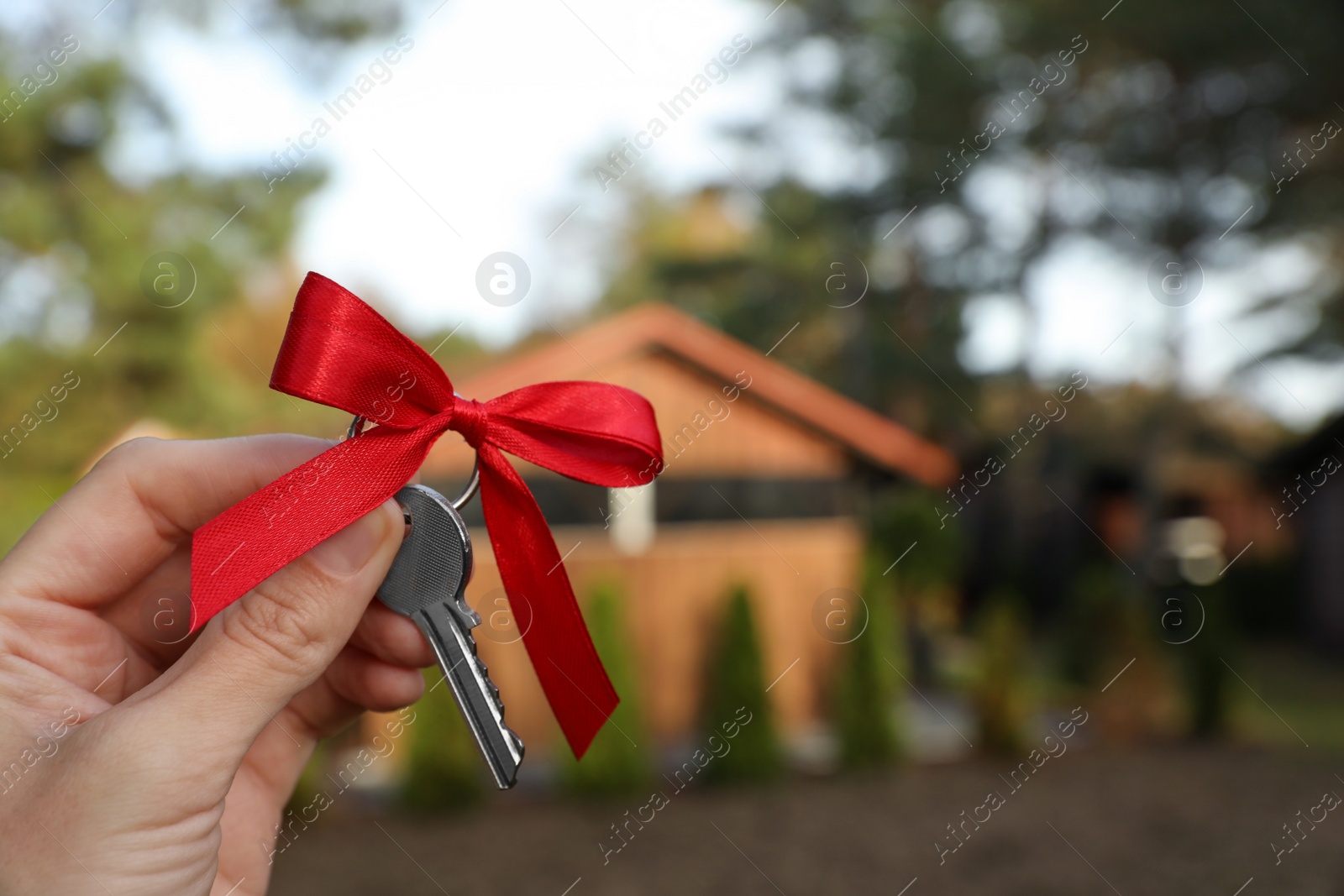 Photo of Woman holding key with bow near house outdoors, closeup. Space for text