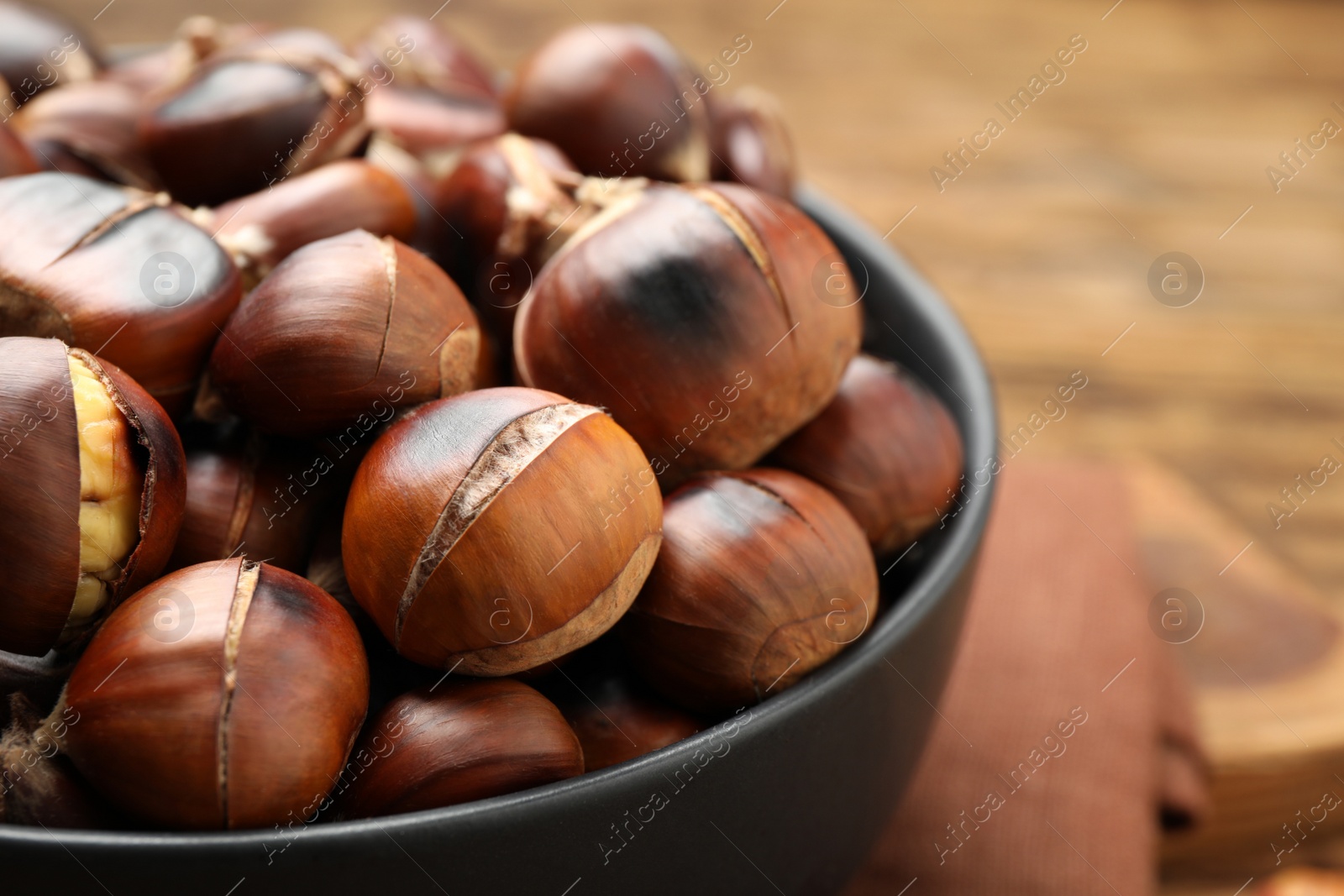 Photo of Delicious roasted edible chestnuts in bowl on table, closeup