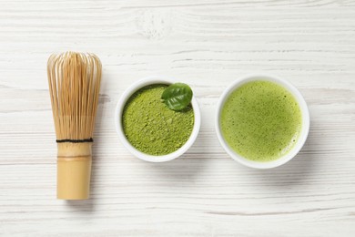 Cup of fresh matcha tea, bamboo whisk and green powder on white wooden table, flat lay