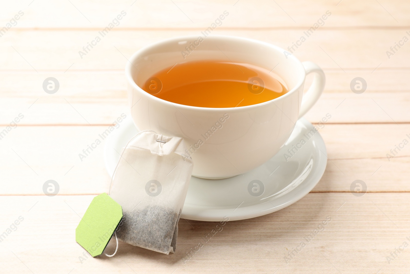 Photo of Tea bag and cup of hot beverage on light wooden table, closeup