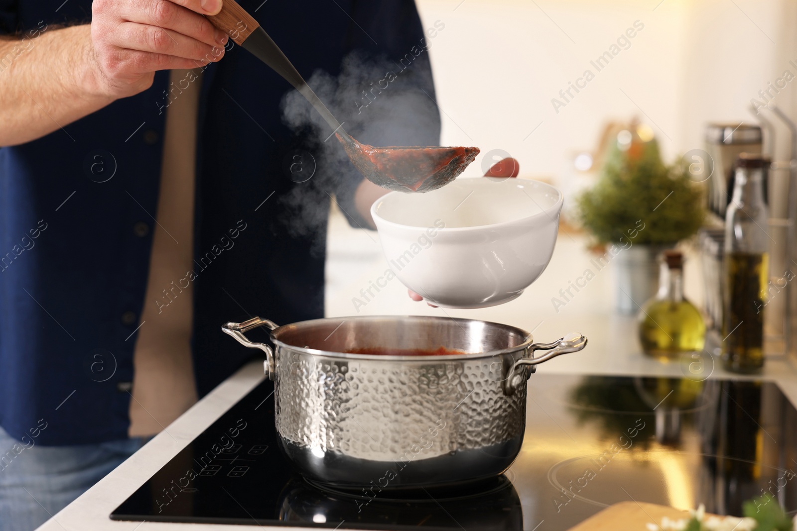 Photo of Man pouring delicious tomato soup into bowl in kitchen, closeup