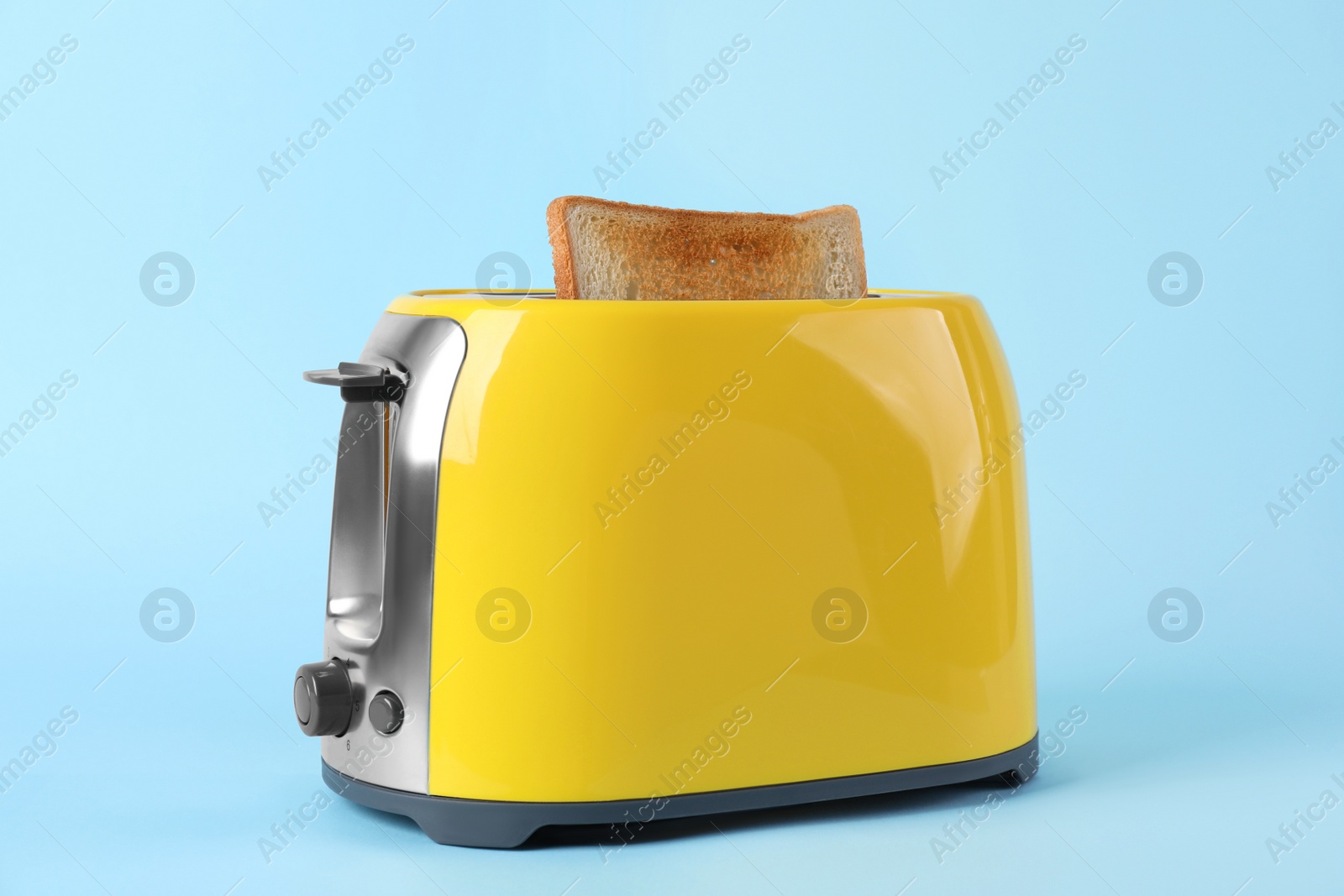 Photo of Modern toaster with slice of bread on light blue background