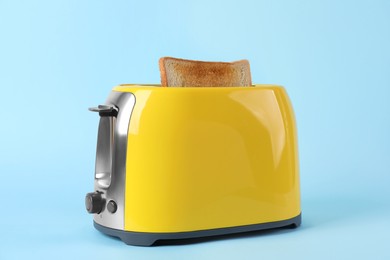 Photo of Modern toaster with slice of bread on light blue background