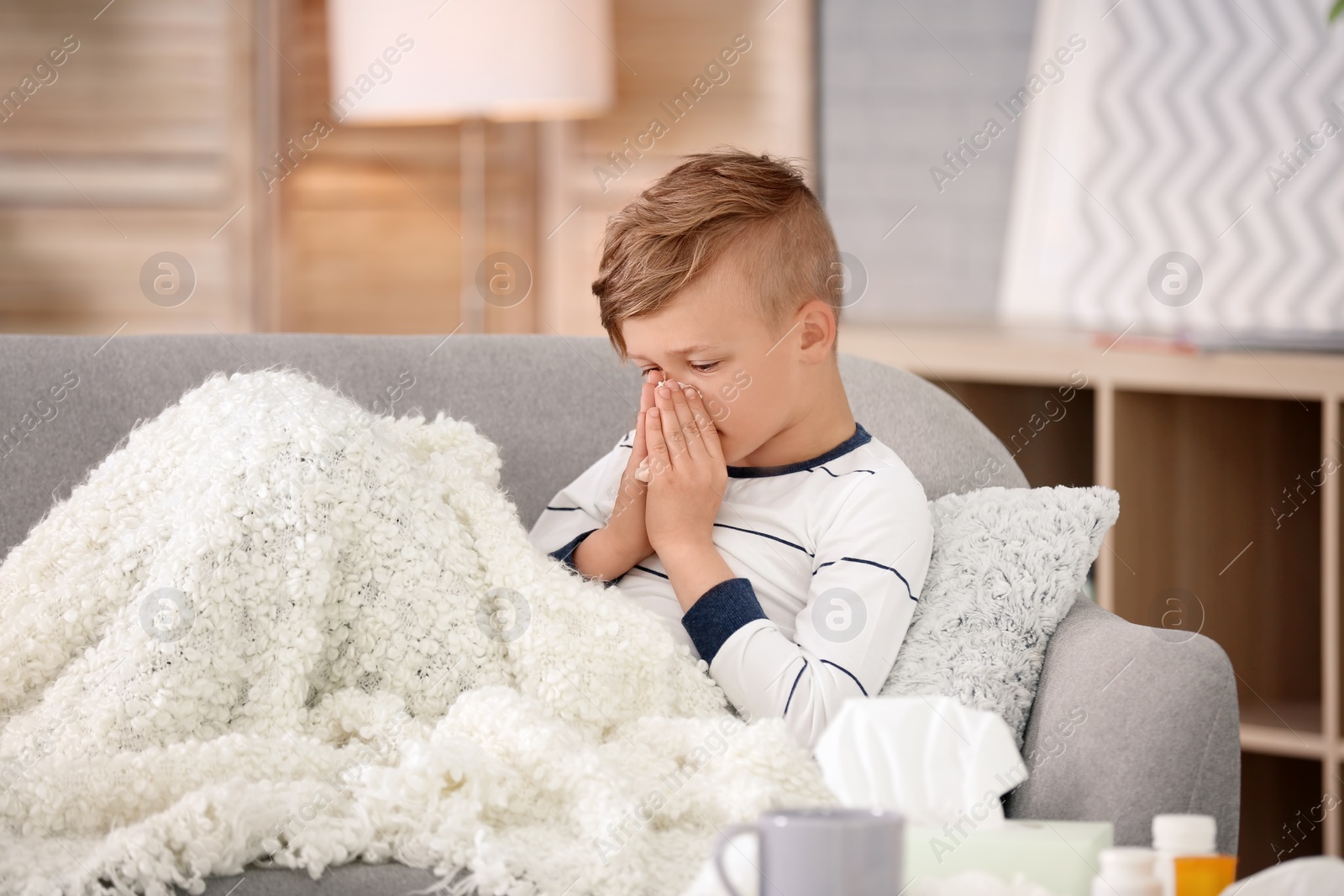 Photo of Little boy with tissue suffering from cold on sofa at home