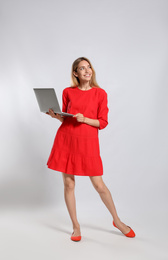 Full length portrait of young woman with modern laptop on light grey background