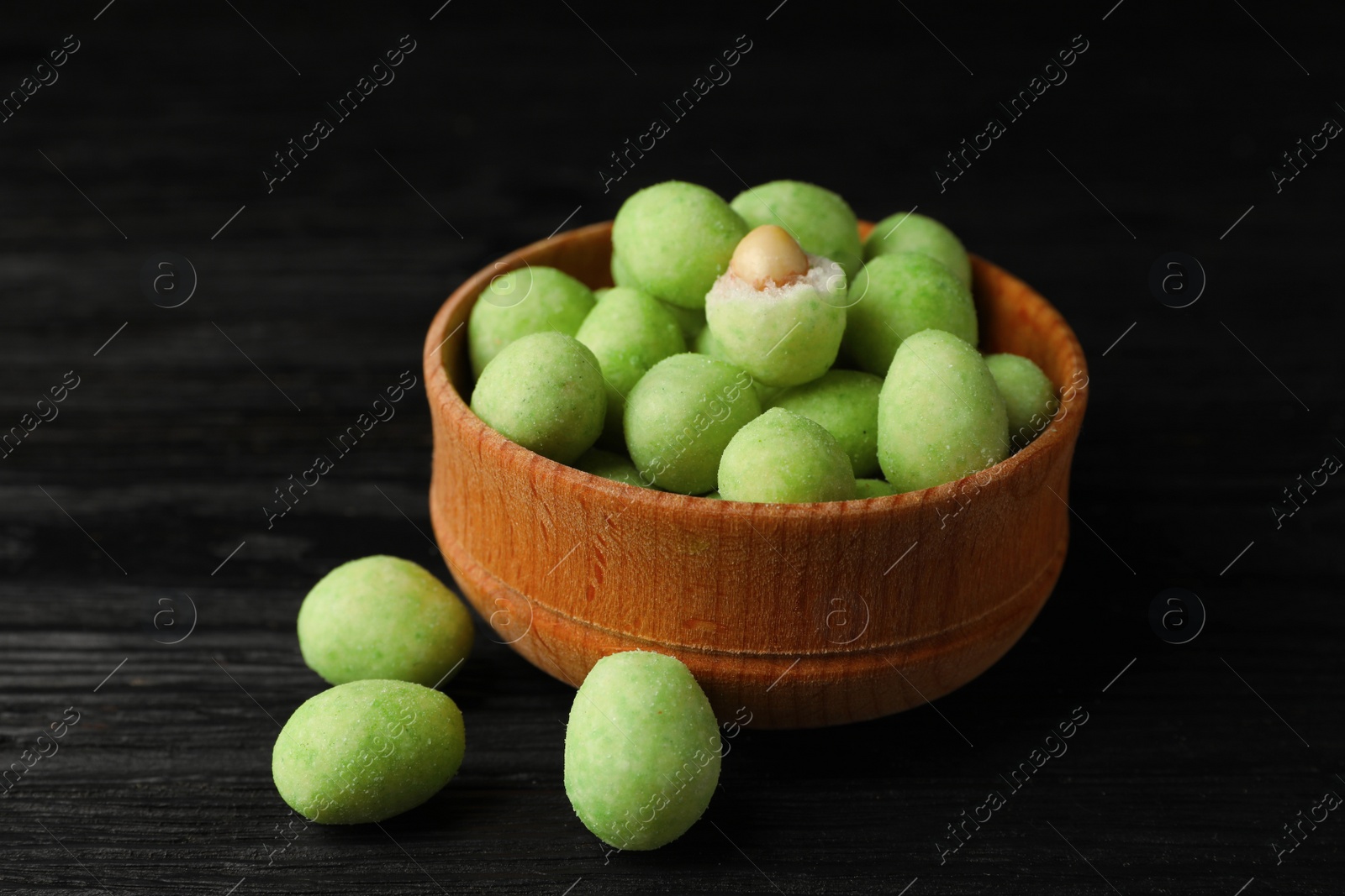 Photo of Tasty wasabi coated peanuts on black wooden table, closeup