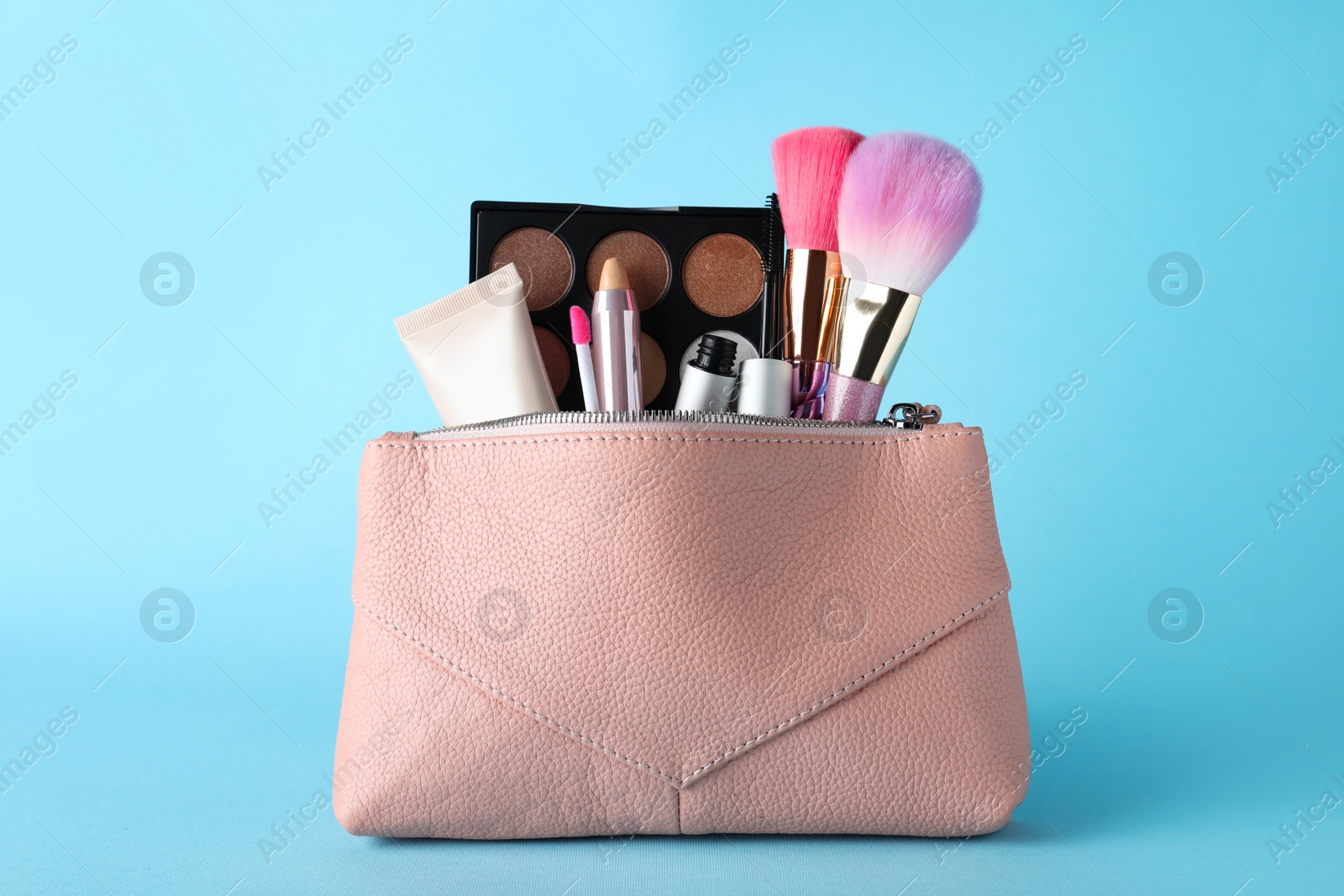 Photo of Cosmetic bag with makeup products and accessories on light blue background