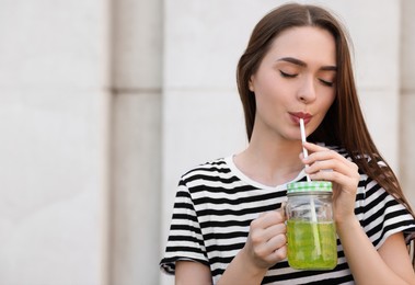 Young woman with mason jar of fresh juice outdoors, space for text
