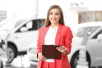 Photo of Young woman with clipboard in car salon