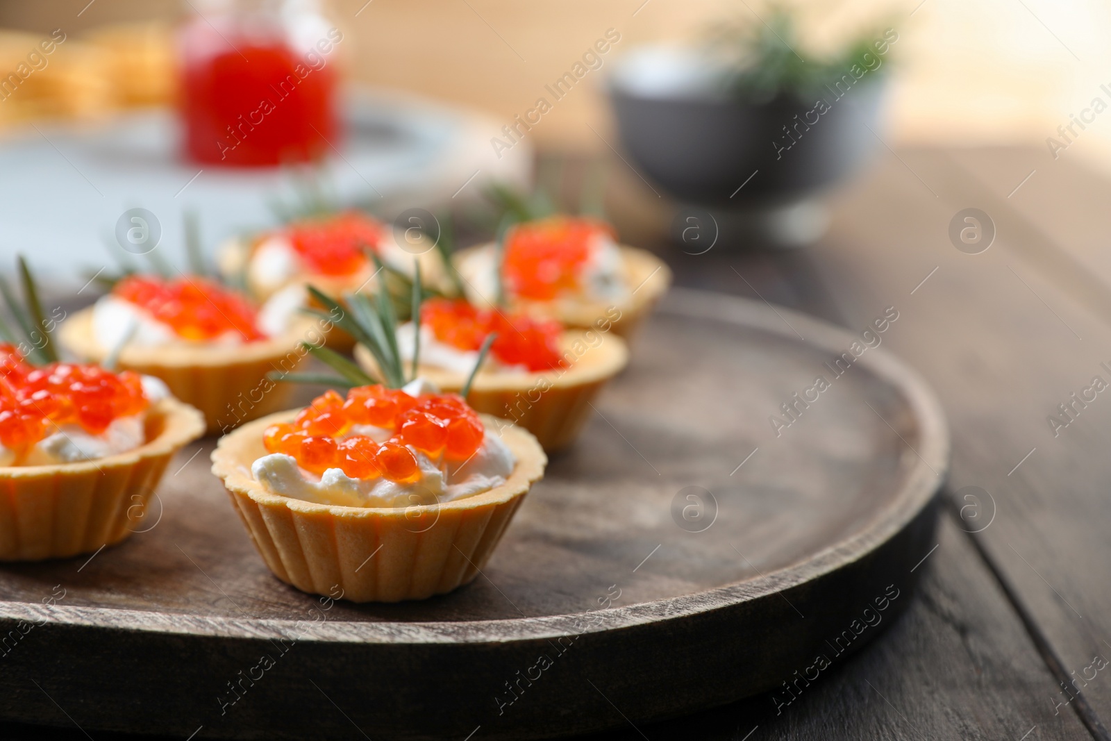 Photo of Delicious tartlets with red caviar and cream cheese served on wooden table, closeup. Space for text