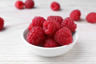 Tasty ripe raspberries in bowl on white wooden table, closeup