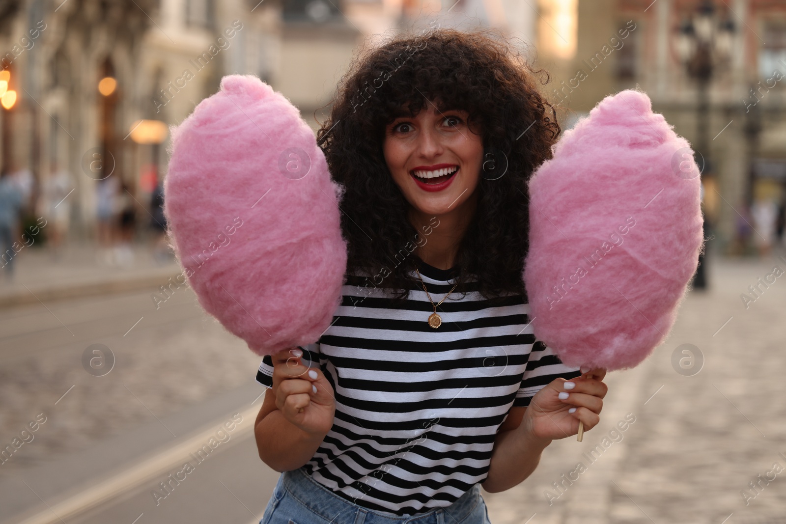 Photo of Portrait of happy woman with pink cotton candies on city street