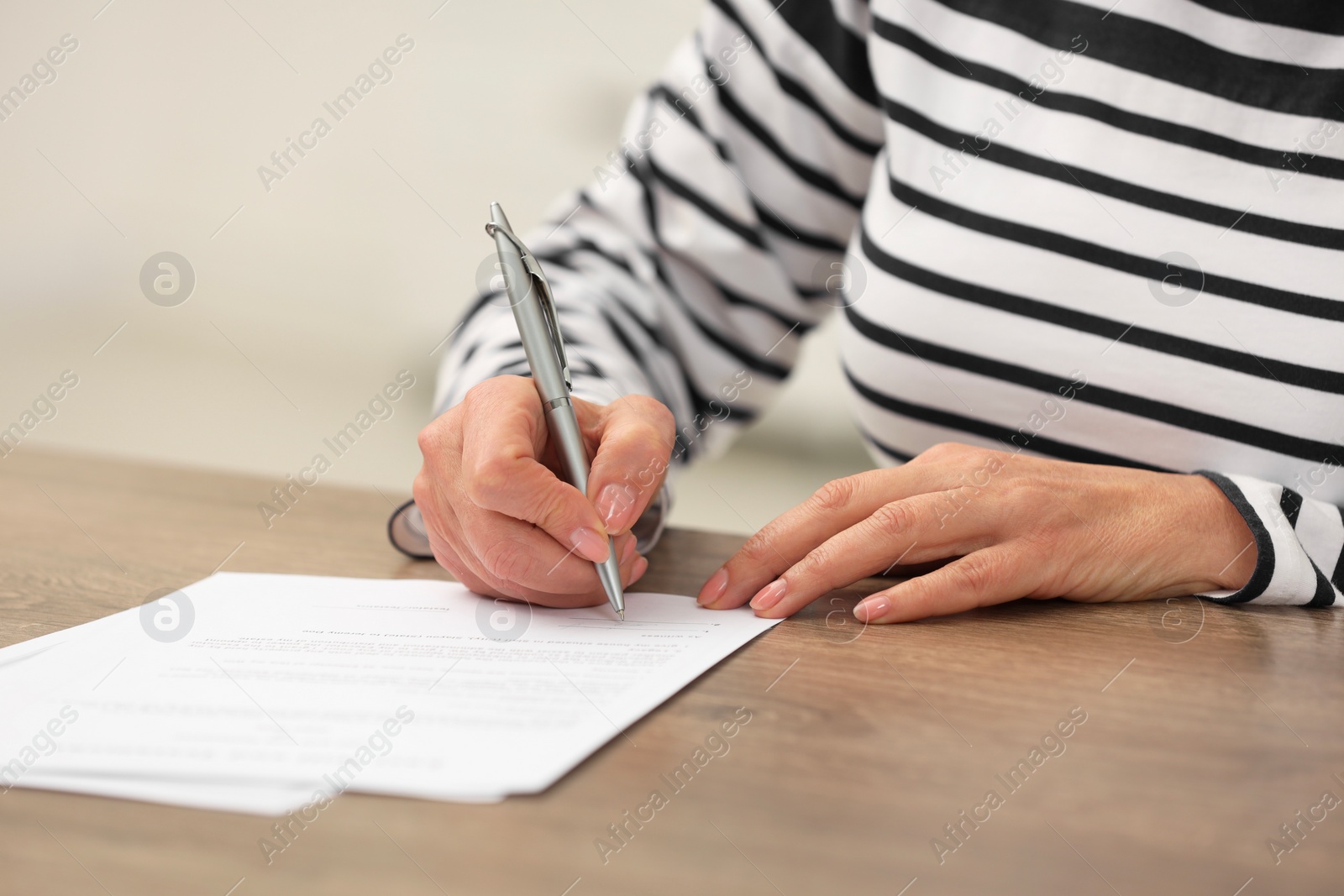 Photo of Senior woman signing Last Will and Testament at wooden table indoors, closeup