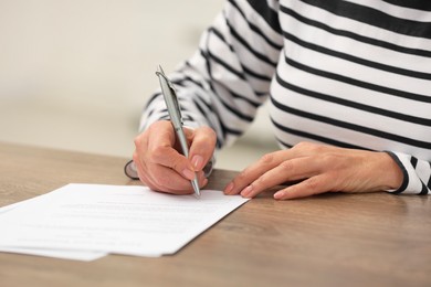 Senior woman signing Last Will and Testament at wooden table indoors, closeup