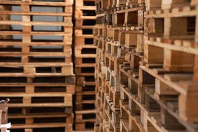 Many empty wooden pallets stacked in warehouse, closeup. Space for text