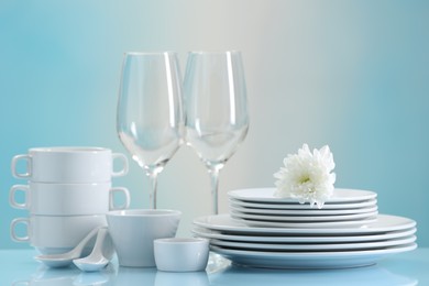 Photo of Set of many clean dishware, flower and glasses on light blue table
