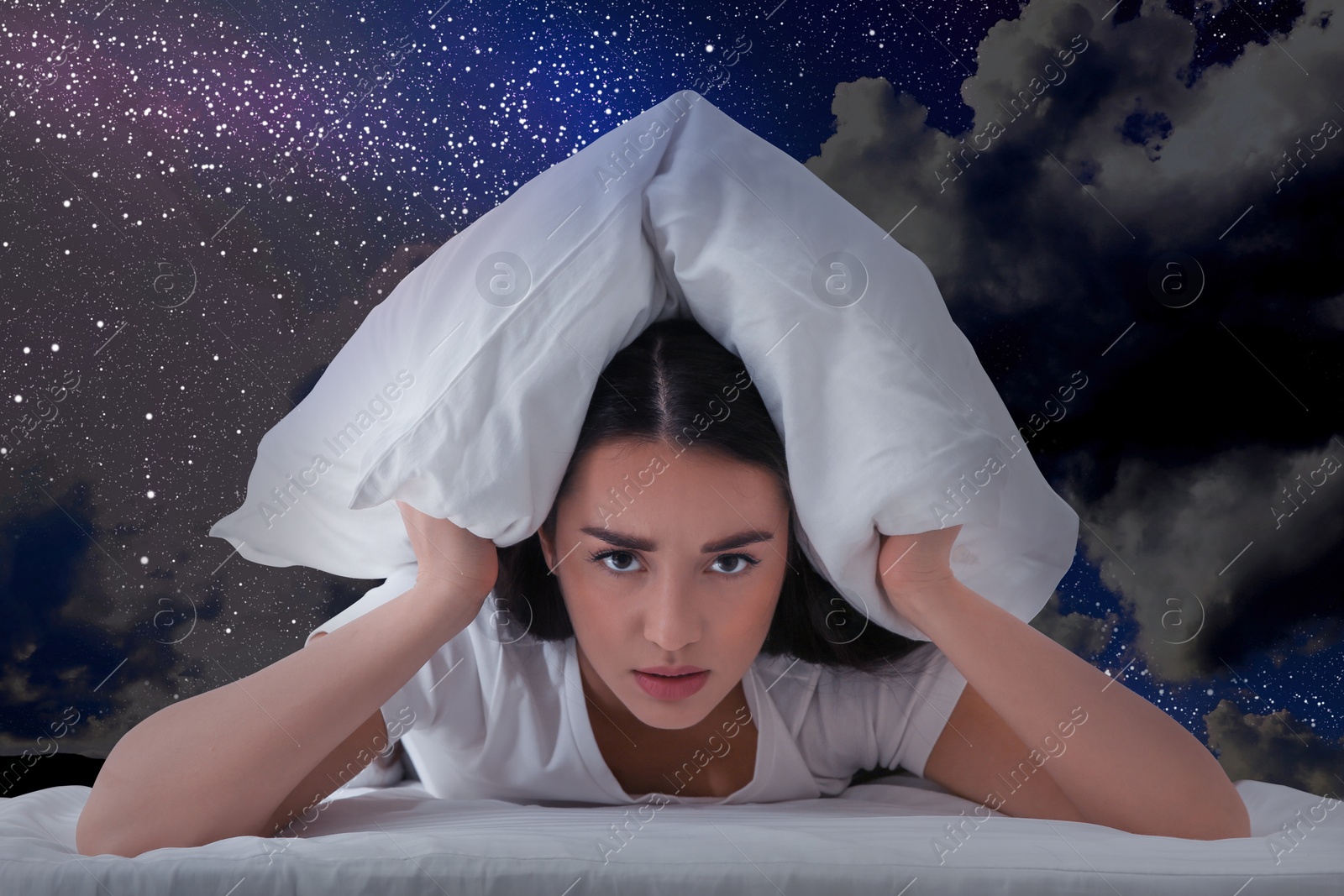 Image of Annoyed young woman covering ears with pillow and beautiful starry sky at night on background