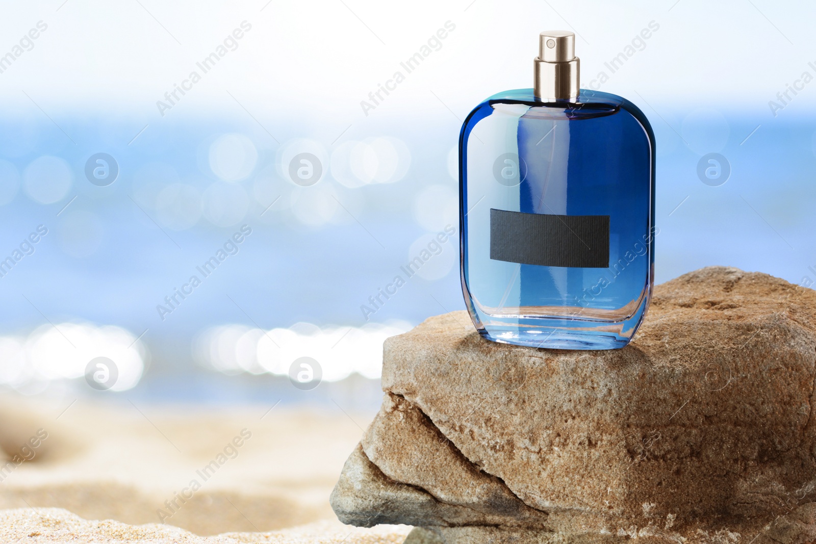 Image of Bottle of aquatic perfume on rock near ocean. Fresh sea breeze scent