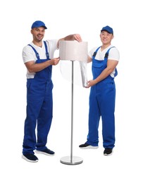 Photo of Workers wrapping lamp in stretch film on white background