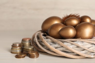 Photo of Golden eggs in nest and coins on white wooden table. Pension concept
