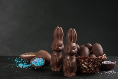 Photo of Chocolate Easter bunnies and eggs on black table. Space for text