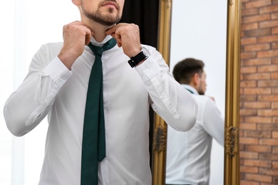 Photo of Businessman adjusting necktie near mirror in room, closeup