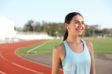 Young sportswoman with wireless earphones at stadium