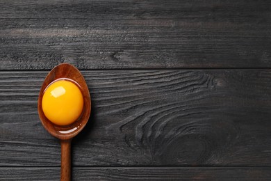 Photo of Spoon with raw egg yolk on black wooden table, top view. Space for text