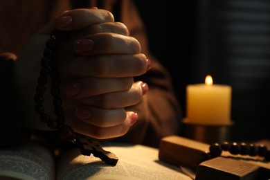 Photo of Woman praying at table with burning candle and Bible, closeup