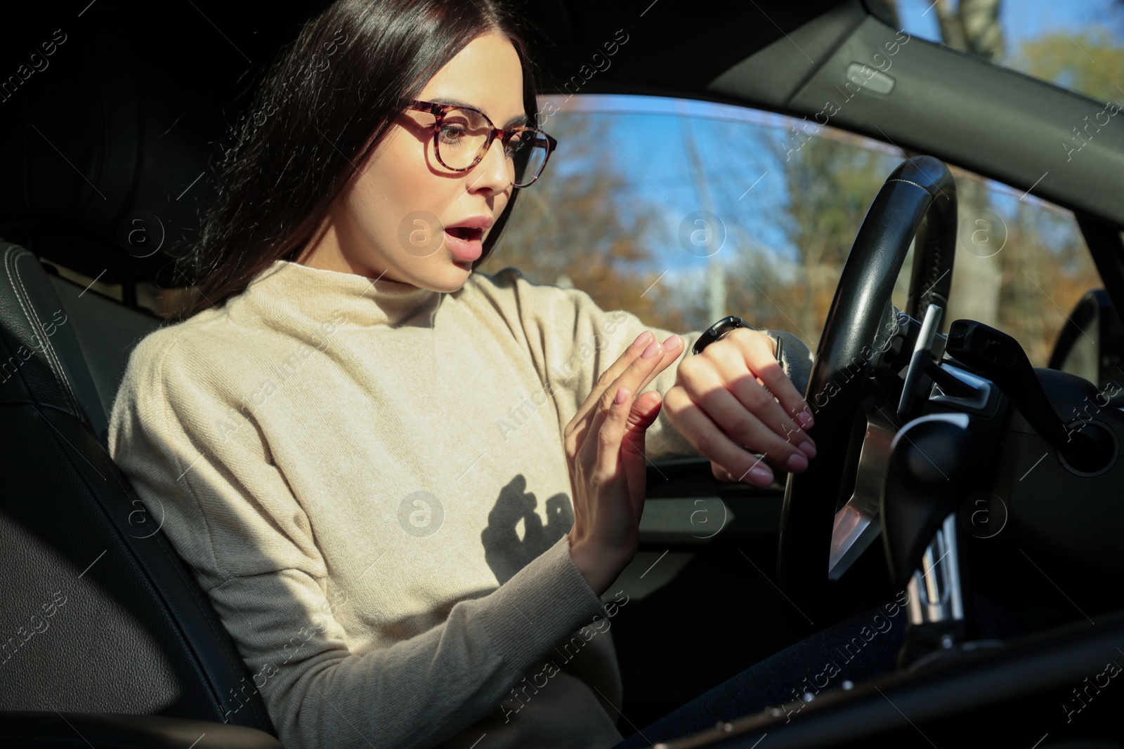 Photo of Emotional woman checking time on watch in car. Being late concept