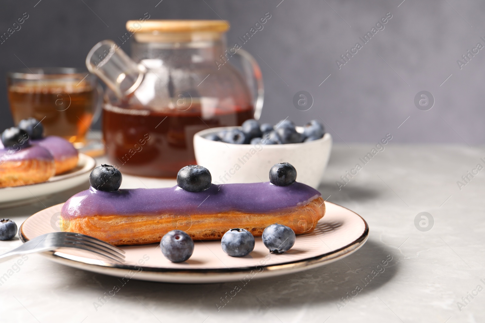 Photo of Tasty glazed eclair with blueberries on grey marble table, closeup