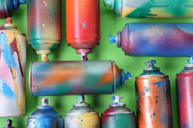 Many spray paint cans on green background, flat lay