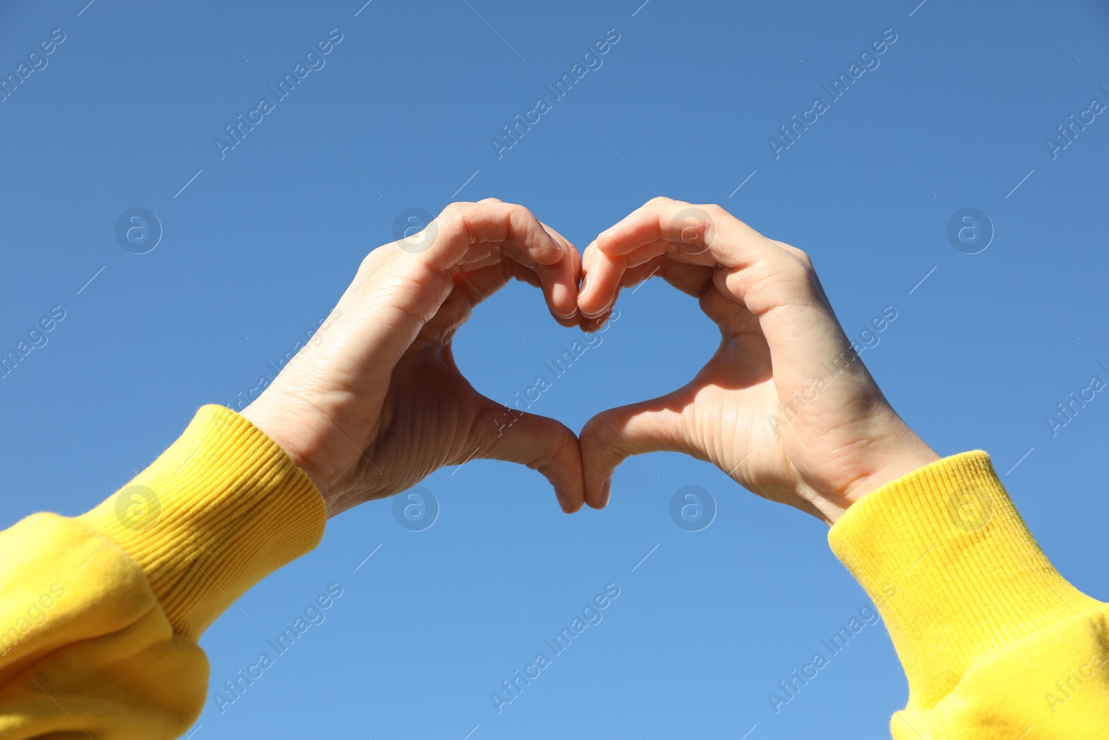 Photo of Woman showing heart against blue sky outdoors on sunny day, closeup of hands
