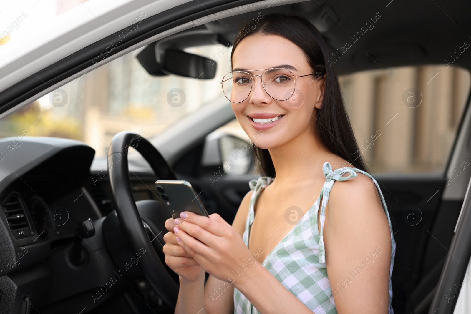 Photo of Happy young woman with smartphone sitting in car