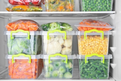 Photo of Containers with deep frozen vegetables in refrigerator