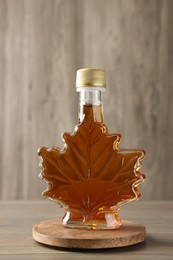 Photo of Leaf shaped bottle of tasty maple syrup on wooden table