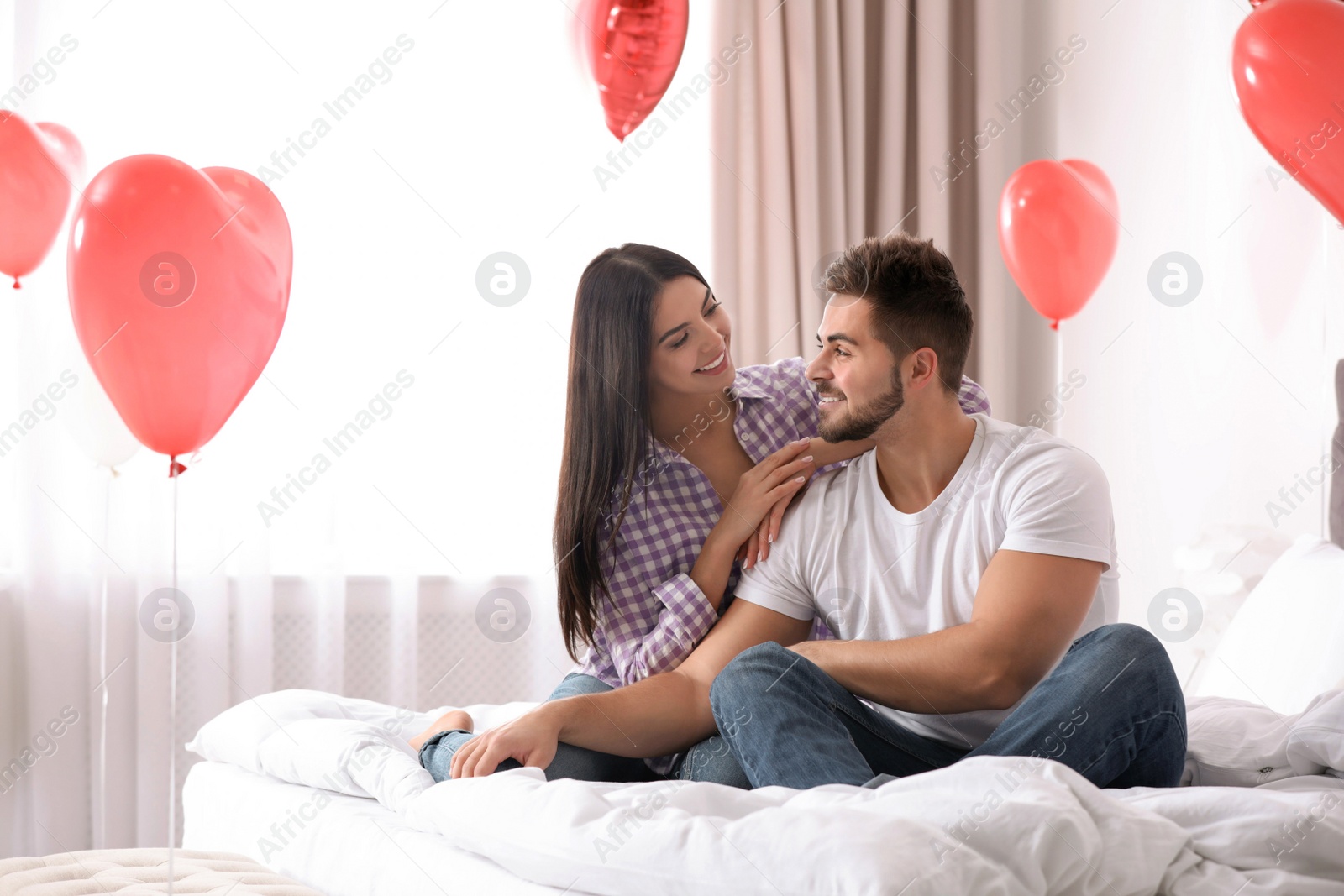 Photo of Lovely young couple in bedroom decorated with heart shaped balloons. Valentine's day celebration