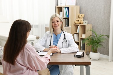 Smiling doctor consulting pregnant patient at table in clinic