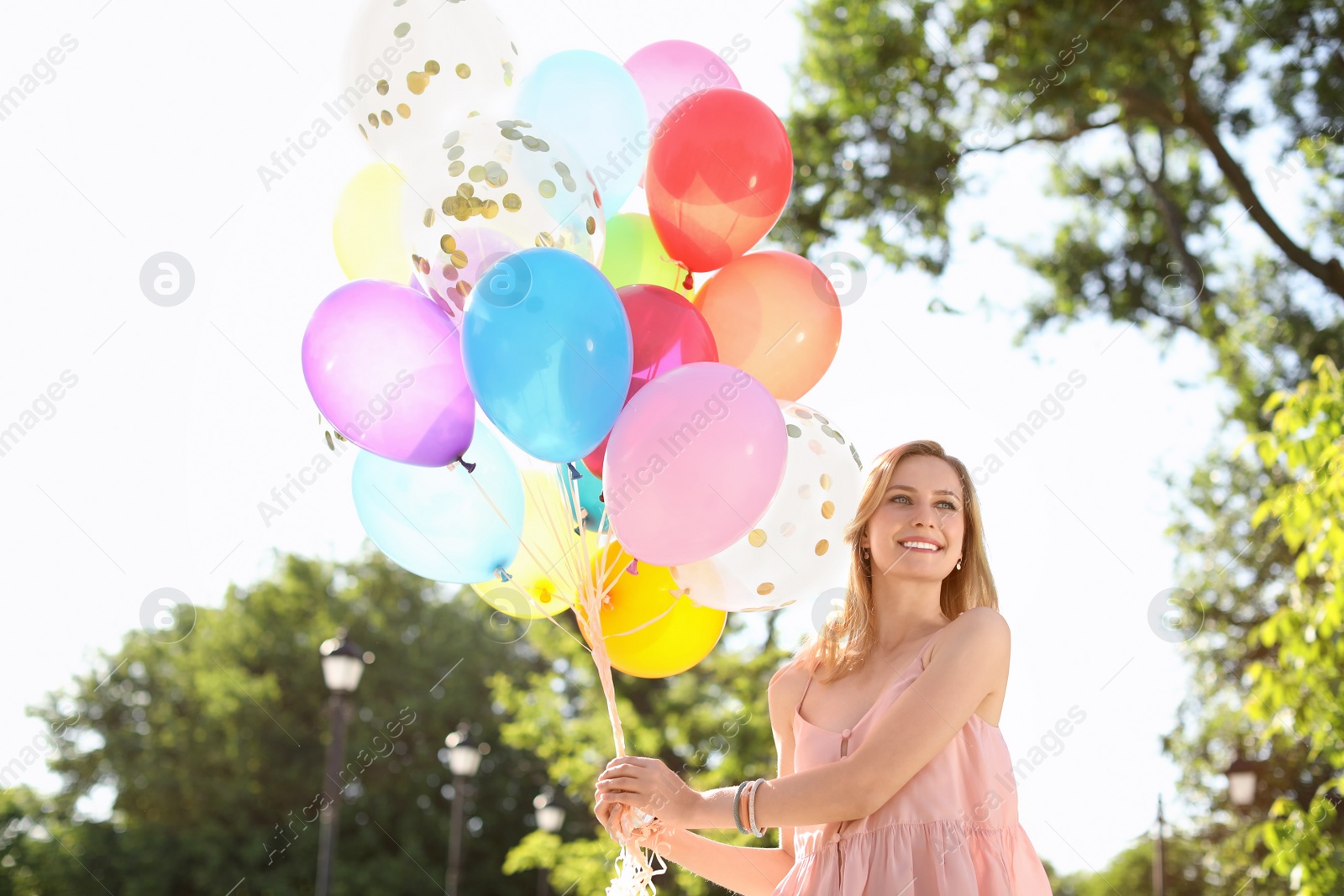 Photo of Young woman with colorful balloons outdoors on sunny day