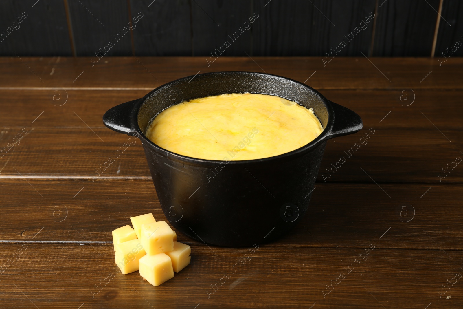 Photo of Fondue pot with melted cheese and pieces at wooden table