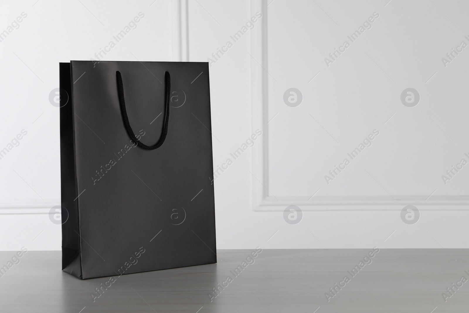 Photo of Black paper bag on white wooden table, space for text