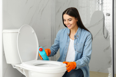 Young woman cleaning toilet bowl in bathroom