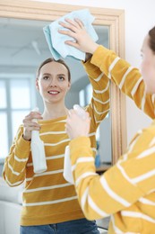 Woman with spay and rag cleaning mirror at home