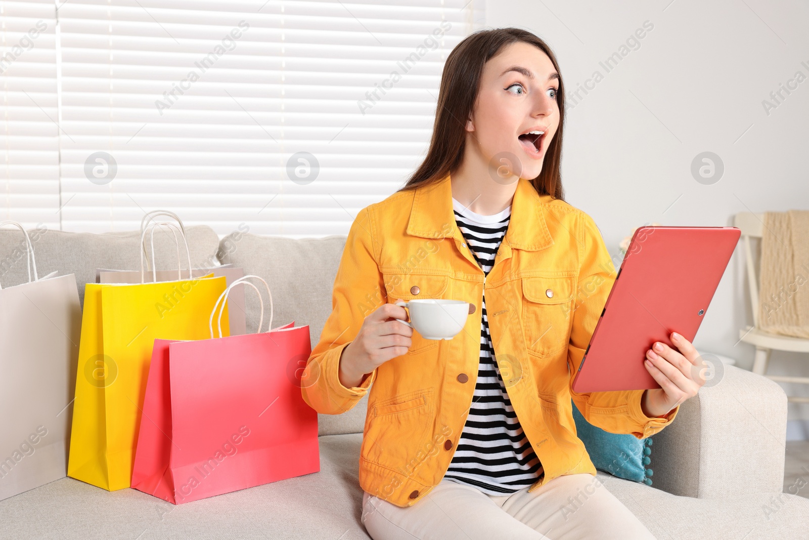 Photo of Special Promotion. Emotional woman holding tablet and cup on sofa indoors