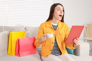 Photo of Special Promotion. Emotional woman holding tablet and cup on sofa indoors