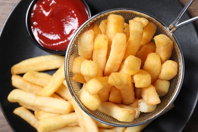 Photo of Delicious French fries and ketchup on black plate, top view