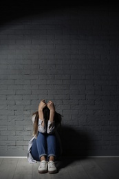 Lonely woman suffering from depression near brick wall