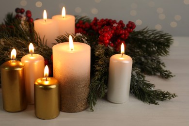 Photo of Different burning candles and Christmas decor on white wooden table